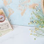 Flat lay of world map, compass, passport, and chamomile flowers, perfect for travel enthusiasts.