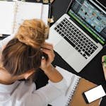 Overhead view of a stressed woman working at a desk with a laptop, phone, and notebooks.