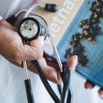 A close-up of a hand holding a stethoscope and a Vietnam travel guide, symbolizing medical care and travel.
