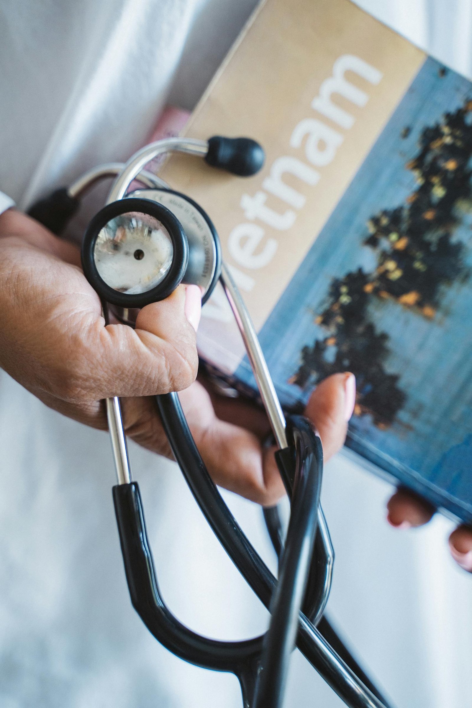 A close-up of a hand holding a stethoscope and a Vietnam travel guide, symbolizing medical care and travel.