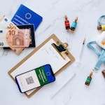 Flat lay of travel essentials including vaccination passport, euros, and medical supplies.