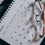 A close-up of a January calendar with eyeglasses on a table, emphasizing planning and organization. - plan a trip