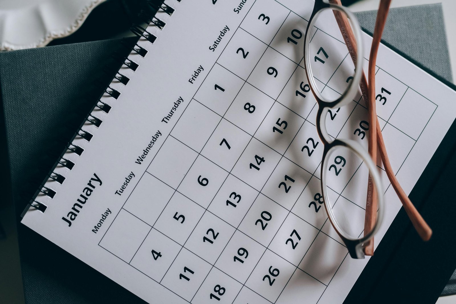 A close-up of a January calendar with eyeglasses on a table, emphasizing planning and organization. - plan a trip