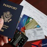 A close-up of a US passport with credit cards, tickets, and a mobile phone on a table. - Passports