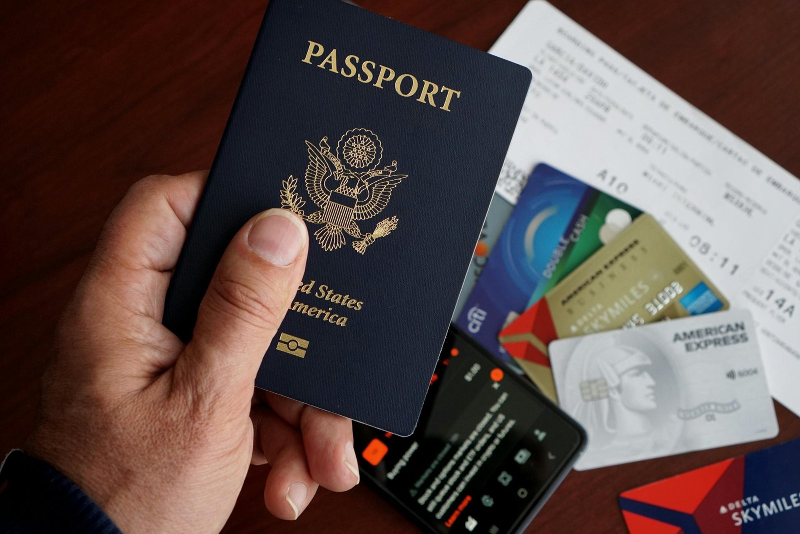 A close-up of a US passport with credit cards, tickets, and a mobile phone on a table. - Passports
