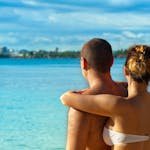 A couple embracing and enjoying the view at a sunny tropical beach, symbolizing love and relaxation. - Honeymoon