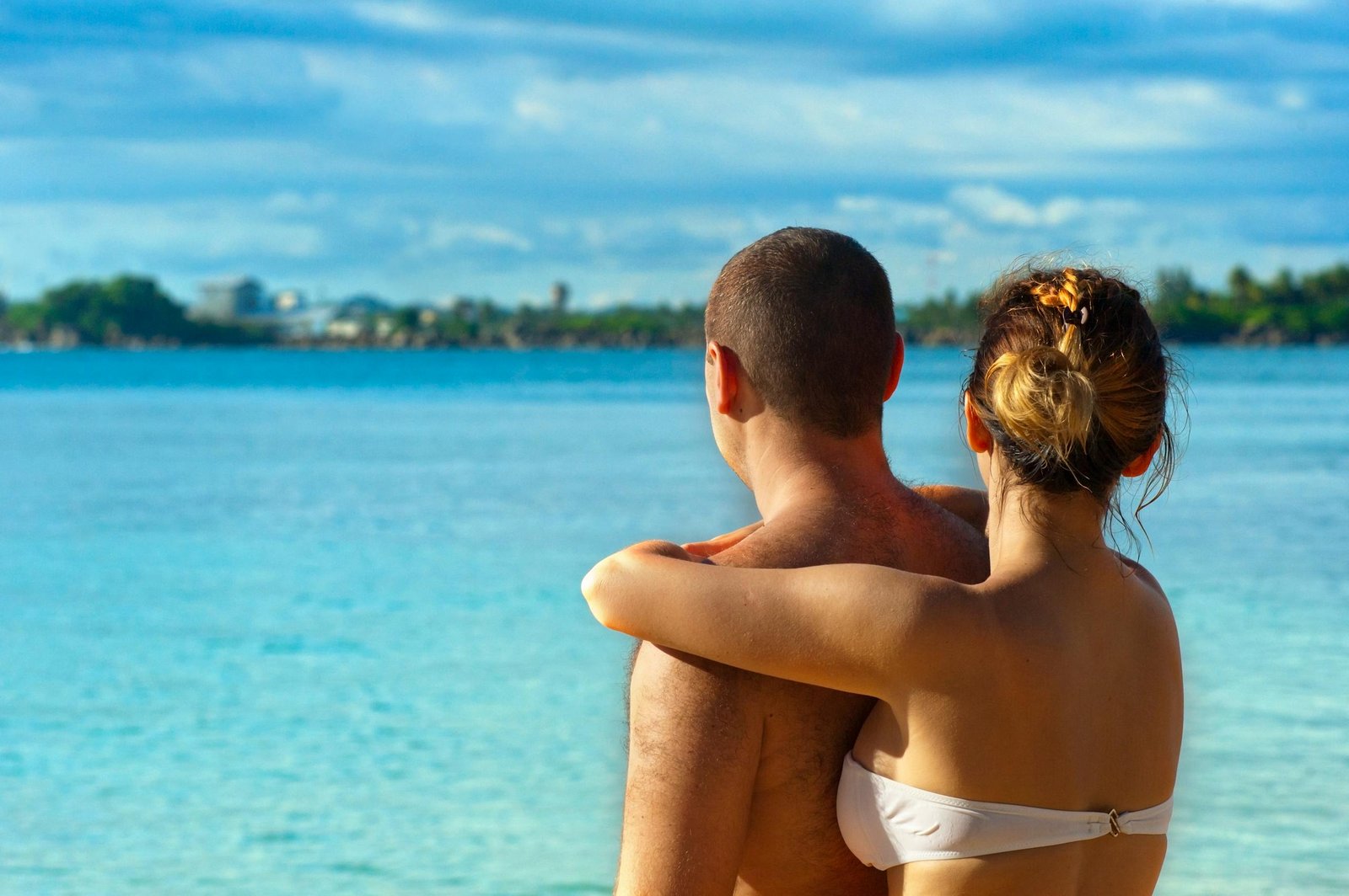 A couple embracing and enjoying the view at a sunny tropical beach, symbolizing love and relaxation. - Honeymoon
