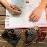 A person planning a journey using a map and vintage camera, evoking travel and exploration. - read travel reviews