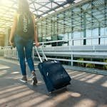 A woman walks with a suitcase outside an airport terminal, ready for travel. CarryOn