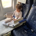 A young girl comfortably sitting in an airplane seat using her mobile device during flight.