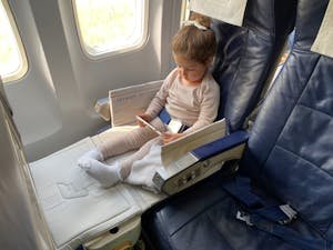 A young girl comfortably sitting in an airplane seat using her mobile device during flight.