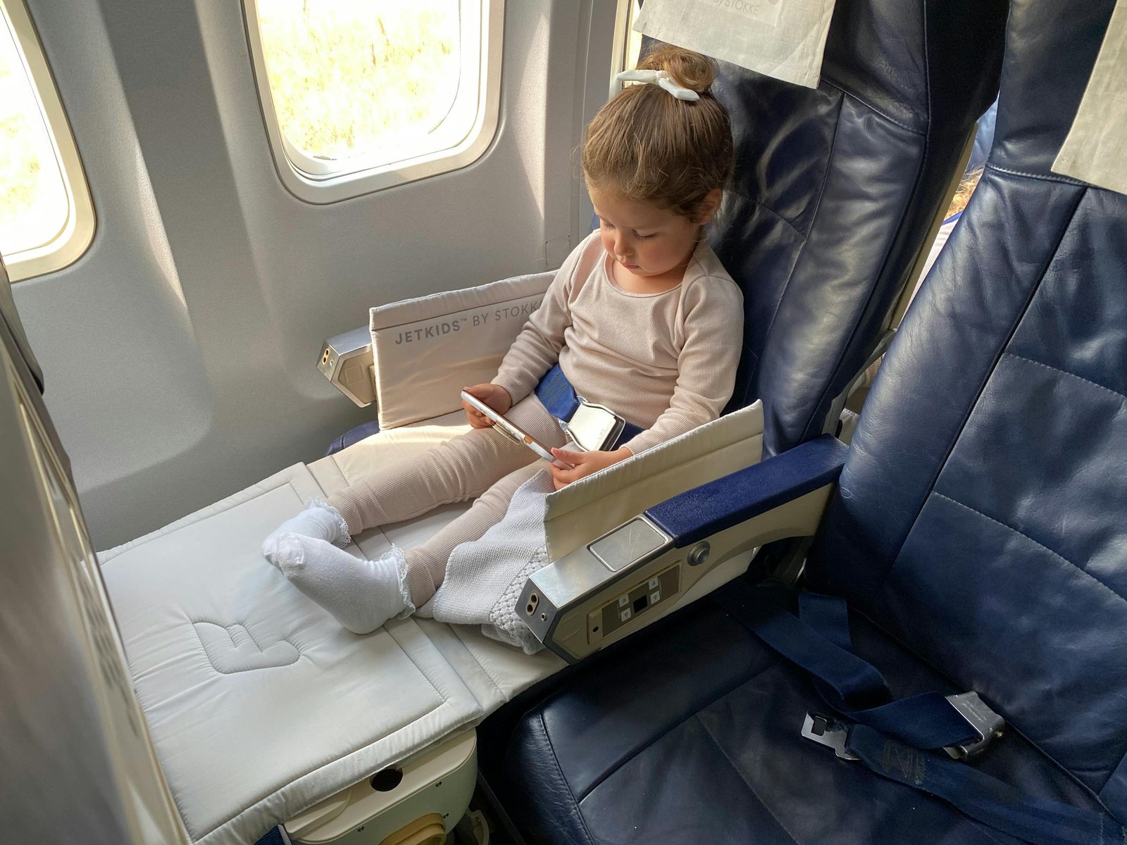 A young girl comfortably sitting in an airplane seat using her mobile device during flight.