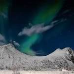 Breathtaking aurora borealis over snow-capped mountains in Myrland, Norway.
