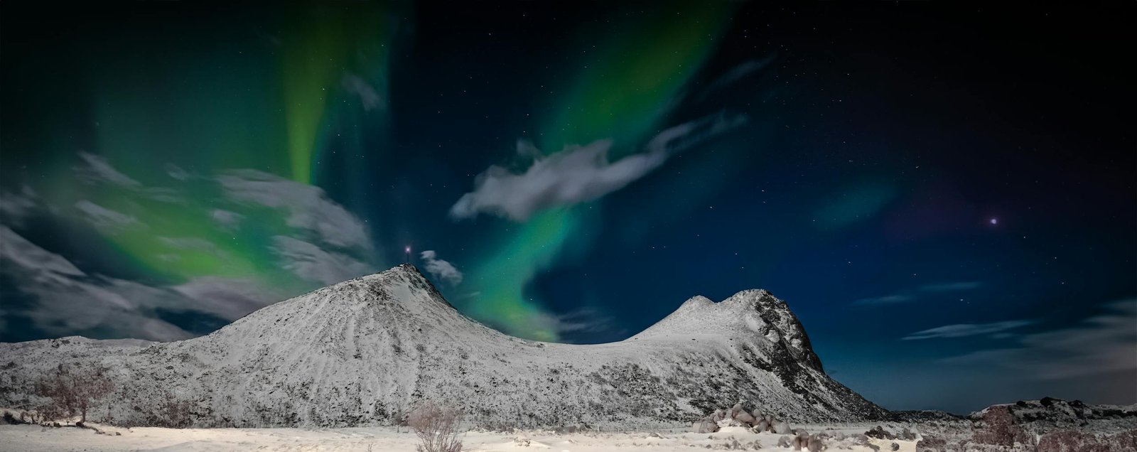 Breathtaking aurora borealis over snow-capped mountains in Myrland, Norway.