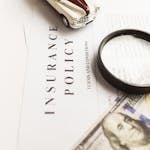 Close-up image of an insurance policy with a magnifying glass, money, and toy car.