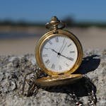 Close-up of an old-fashioned pocket watch resting on a rock at a beach. Travel Time