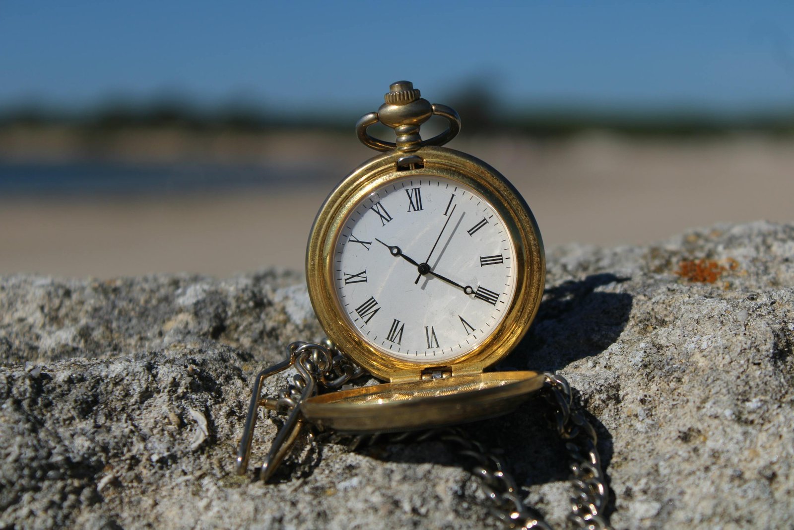 Close-up of an old-fashioned pocket watch resting on a rock at a beach. Travel Time