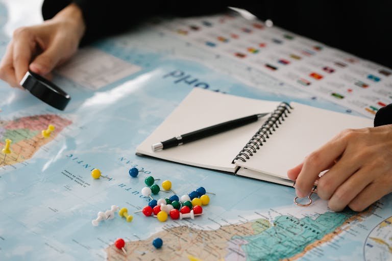 Close-up of hands planning a trip with map, pins, and notebook. travel planning