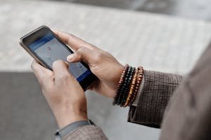 Close-up of hands with bracelets navigating on smartphone using GPS app outdoors. Travel Planning