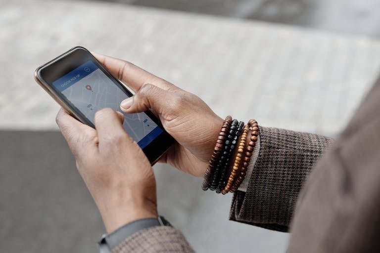 Close-up of hands with bracelets navigating on smartphone using GPS app outdoors. Travel Planning