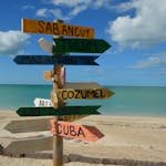 Colorful signpost on a sunny beach, pointing to popular vacation destinations.