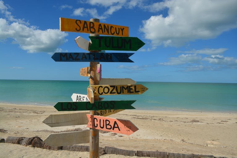Colorful signpost on a sunny beach, pointing to popular vacation destinations.