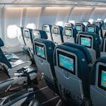 Empty airplane interior highlighting rows of seats with touchscreens, offering a modern in-flight experience. - Compare Flight Options
