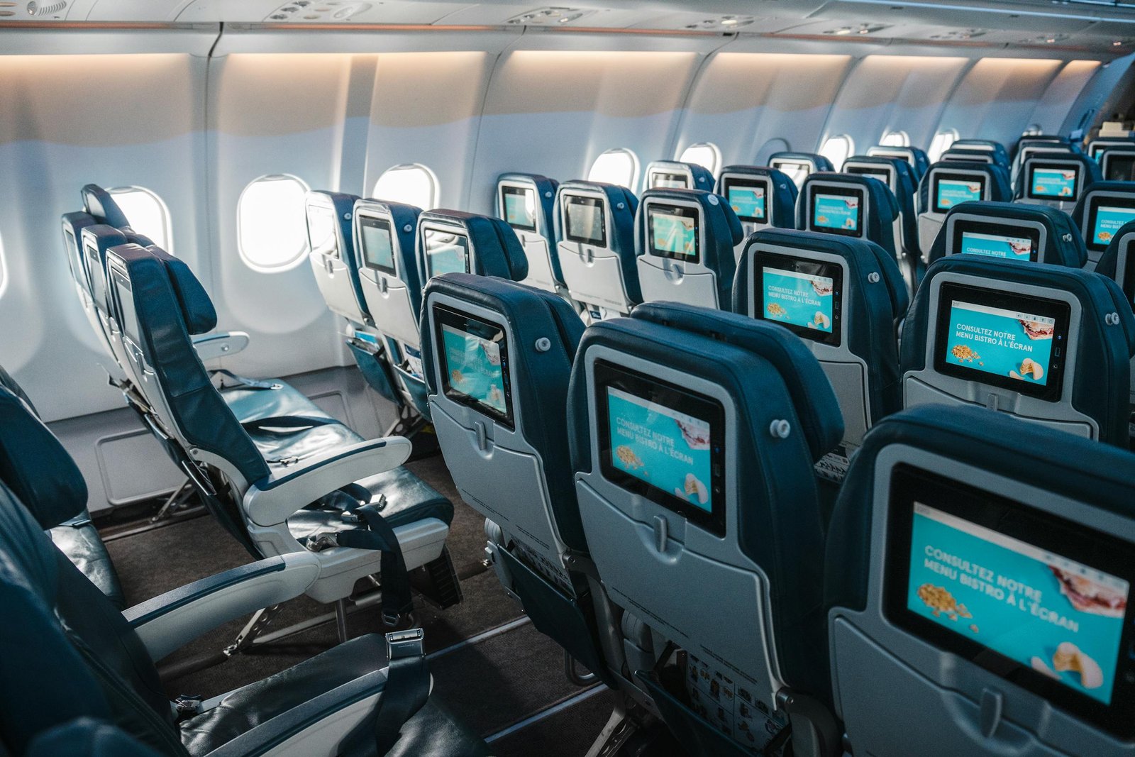 Empty airplane interior highlighting rows of seats with touchscreens, offering a modern in-flight experience. - Compare Flight Options
