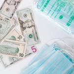 From above composition of stack of USA dollar bills placed near medical protective masks produced in China illustrating concept of medical expenses and deficit during COVID 19