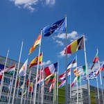 Low angle view of European Union flags on flagpoles against a blue sky, symbolizing unity. International Travel