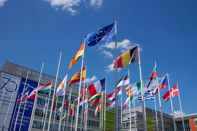 Low angle view of European Union flags on flagpoles against a blue sky, symbolizing unity. International Travel