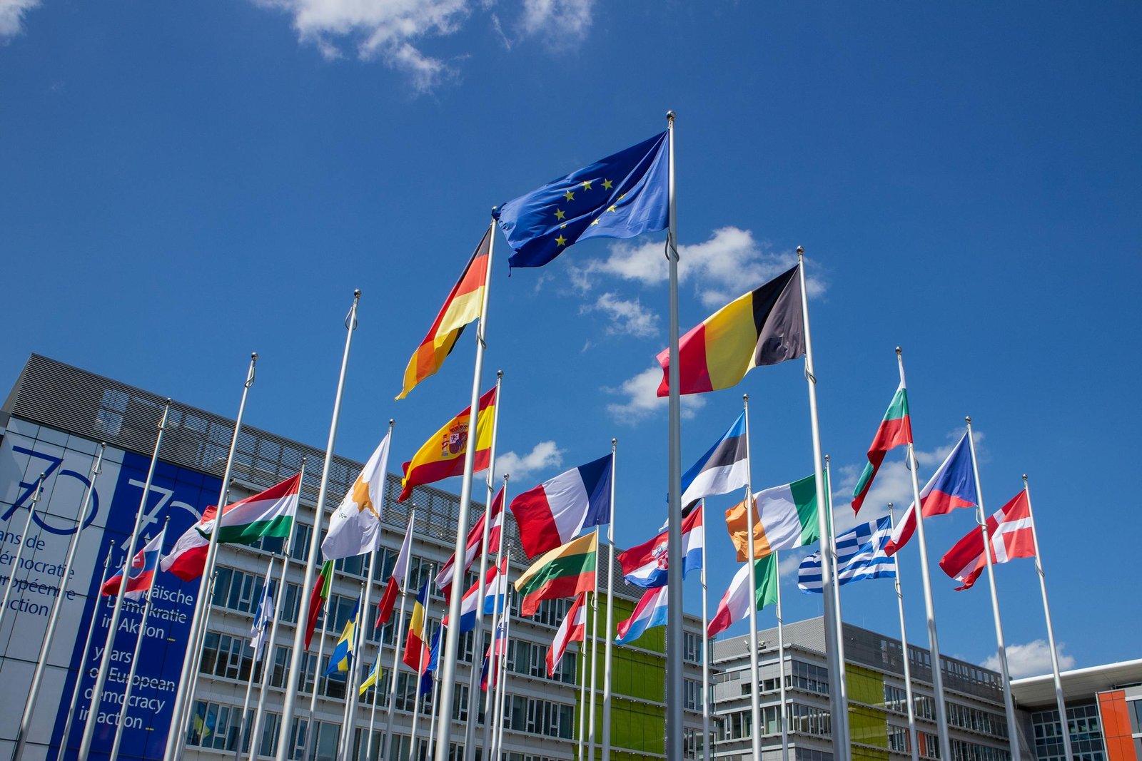 Low angle view of European Union flags on flagpoles against a blue sky, symbolizing unity. International Travel