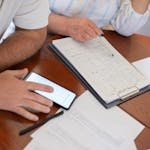 Senior couple examining bills and documents with smartphone and clipboard at home. -travel budget