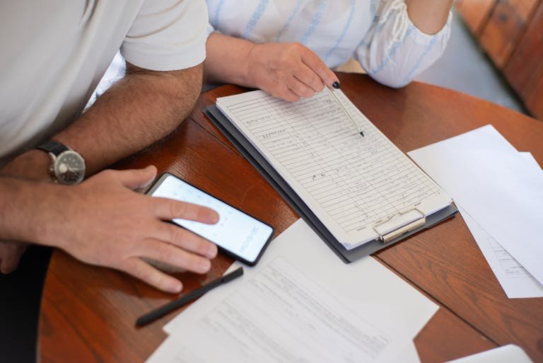 Senior couple examining bills and documents with smartphone and clipboard at home. -travel budget