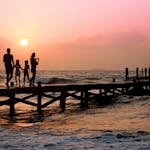 Silhouetted family enjoys a stroll on the beach pier at a vibrant sunset over the ocean waves. - Family Vacation