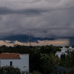 Stormy clouds loom over a cityscape, highlighting a dramatic sky and weather phenomena.