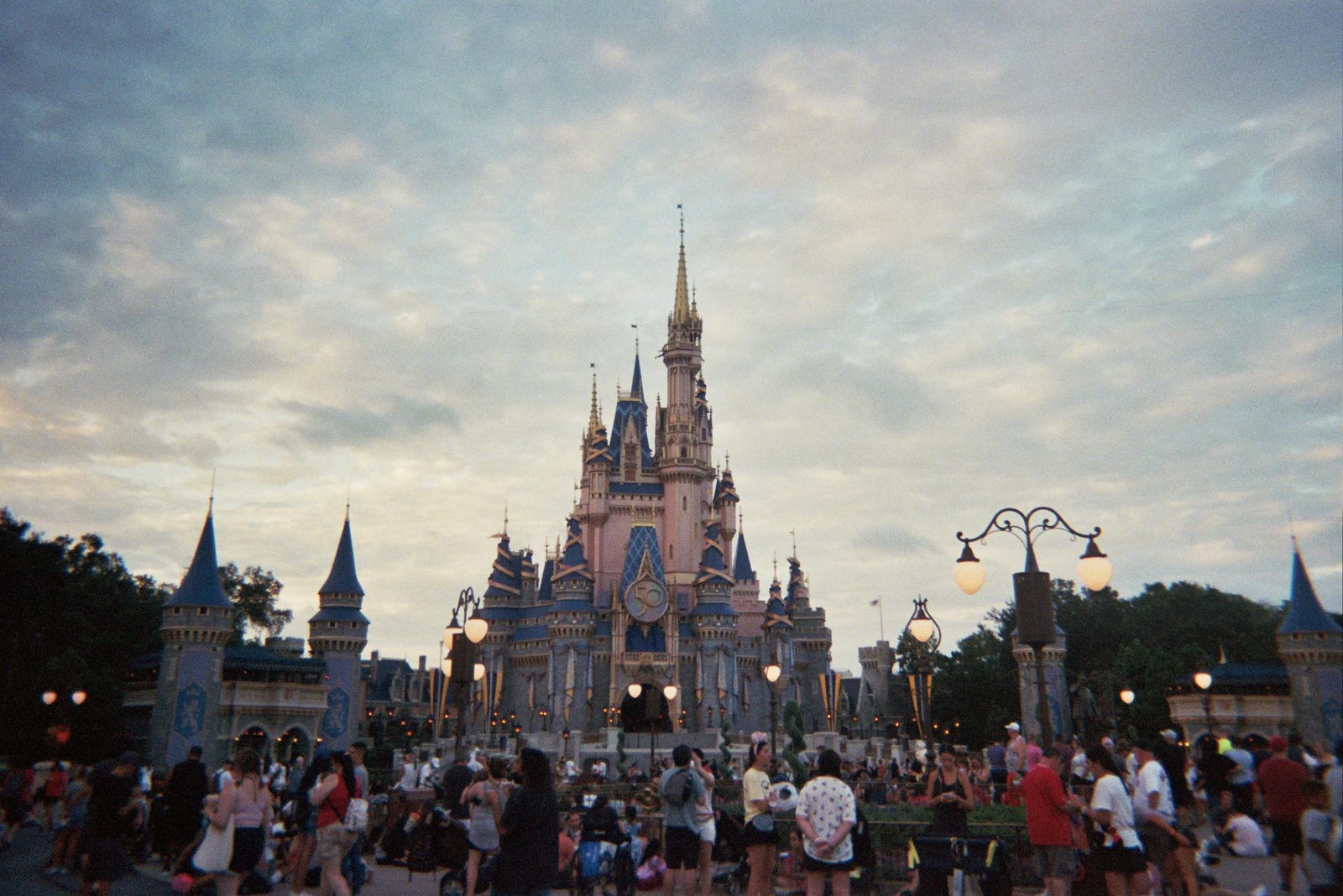 Tourists gather around Cinderella's Castle at Walt Disney World during sunset, capturing a magical moment. - Disney Vacation