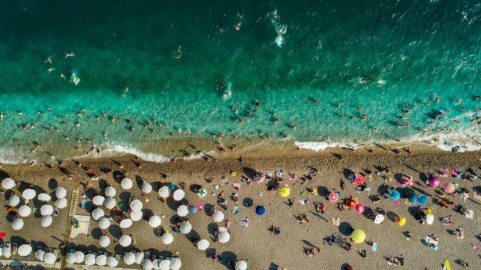 Vibrant summer scene on Antalya's Konyaalti Beach with turquoise waters and colorful umbrellas.