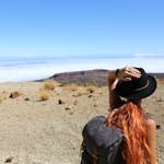 Woman standing in a desert landscape, looking at distant mountains, wearing a hat and backpack. Solo Travel
