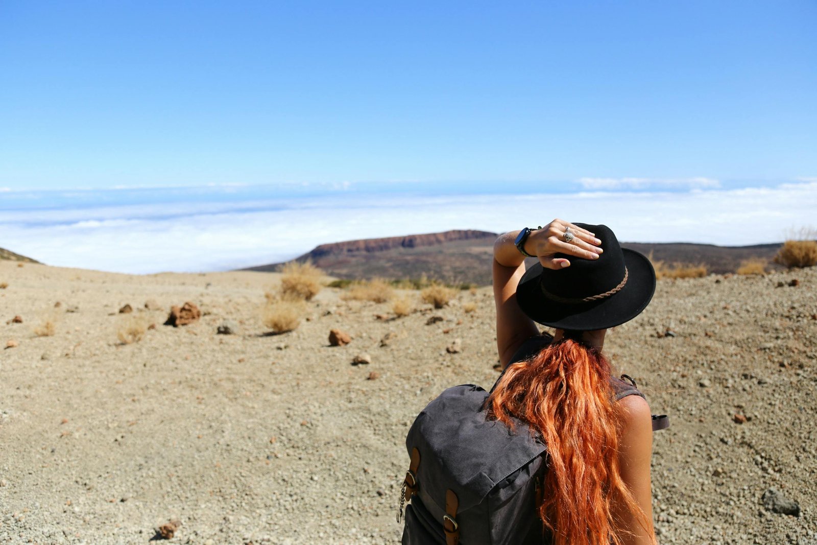 Woman standing in a desert landscape, looking at distant mountains, wearing a hat and backpack. Solo Travel