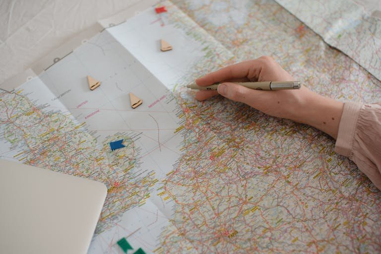 Hand holding pen over Europe map, planning travel route with markers.