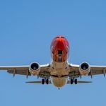A red commercial airplane captured landing against a clear blue sky at Manises Airport, Spain.