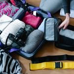 Portugal Travel Checklist: What to Pack 6 A woman arranging clothes and accessories into a suitcase, preparing for travel.