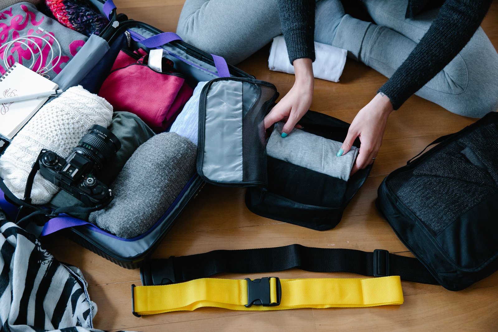 Portugal Travel Checklist: What to Pack 1 A woman arranging clothes and accessories into a suitcase, preparing for travel.