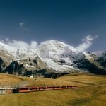 Captivating view of a red train traversing snowcapped Alps, under a clear blue sky.