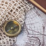 Flat lay of a vintage compass and leather notebook on a retro maritime map.