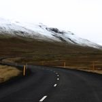 Winding road in Iceland with snow-covered mountains and open landscape, ideal for travel inspiration.