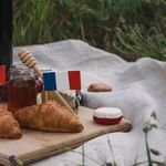A delightful French picnic setup with croissants, cheese, grapes, and red wine outdoors.