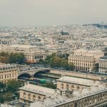 Paris vs. South of France: First Trip? 2 Aerial view of Paris cityscape featuring Seine River and historic architecture under a cloudy sky.