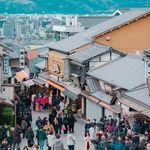 Crowds walk through a vibrant street in a historic Japanese town, full of traditional architecture.